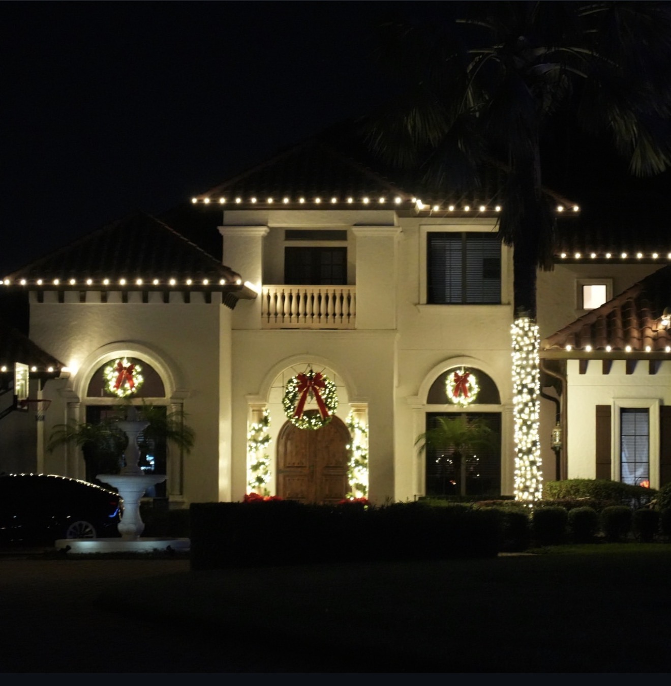 Warm white roofline lights, wreaths and garland around an arched entry